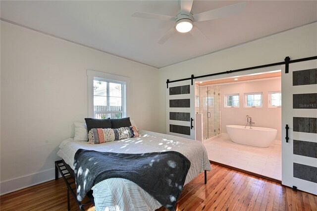 bedroom with a barn door, connected bathroom, hardwood / wood-style floors, and baseboards