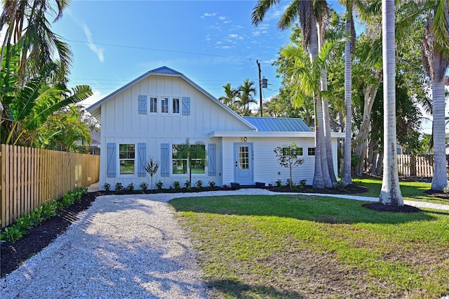 modern inspired farmhouse with gravel driveway, board and batten siding, metal roof, fence, and a front lawn