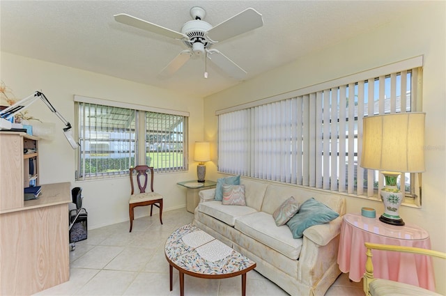 living area featuring light tile patterned floors, ceiling fan, a textured ceiling, and baseboards