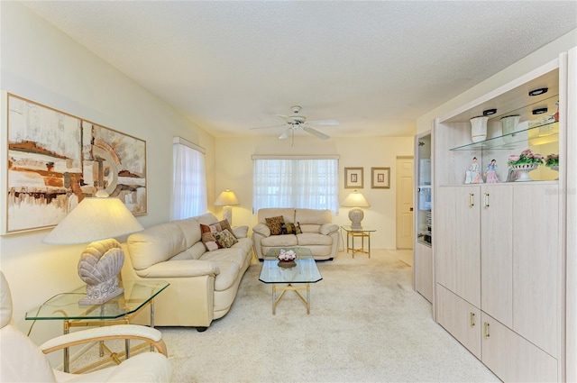 living area featuring light colored carpet, ceiling fan, and a textured ceiling