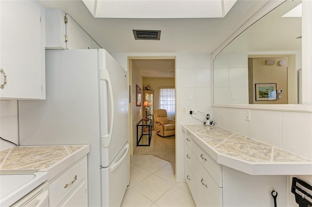 kitchen featuring light tile patterned floors, visible vents, freestanding refrigerator, light carpet, and white cabinetry