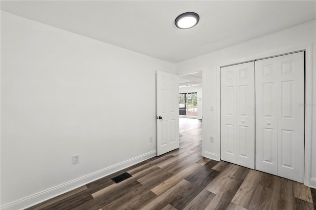 unfurnished bedroom with dark wood-style flooring, a closet, visible vents, and baseboards