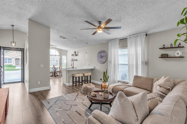 living room with lofted ceiling, visible vents, a ceiling fan, a textured ceiling, and wood finished floors