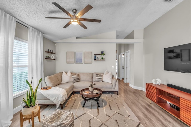 living area with lofted ceiling, a textured ceiling, a ceiling fan, baseboards, and light wood-style floors