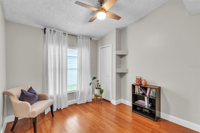 living area featuring a textured ceiling, light wood finished floors, a ceiling fan, and baseboards