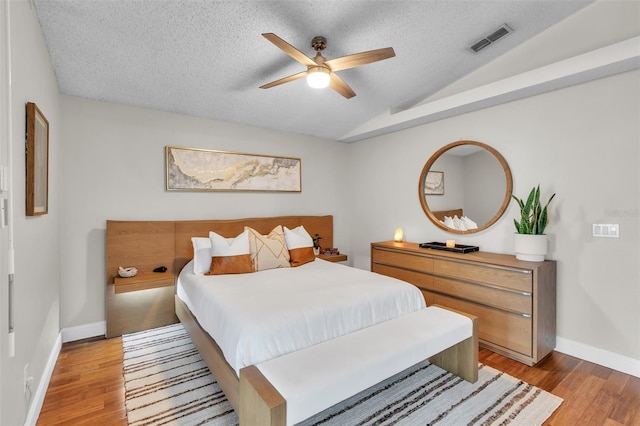 bedroom featuring light wood finished floors, baseboards, visible vents, lofted ceiling, and a textured ceiling