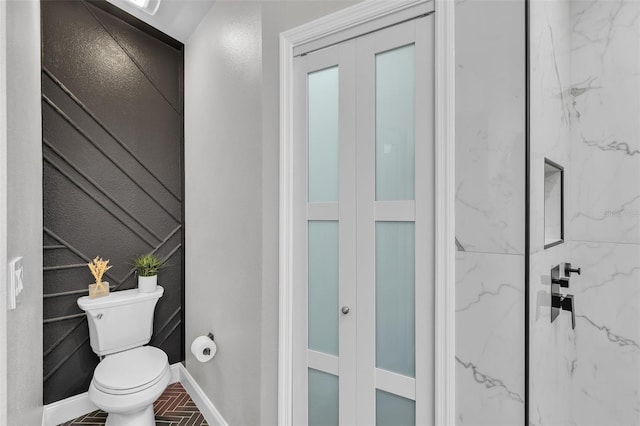 full bathroom with toilet, brick floor, a marble finish shower, and baseboards