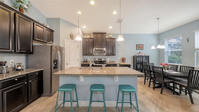 kitchen featuring a kitchen island with sink, stainless steel appliances, a sink, light stone countertops, and pendant lighting