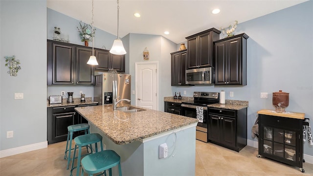 kitchen featuring light stone counters, stainless steel appliances, a kitchen island with sink, a sink, and a kitchen bar