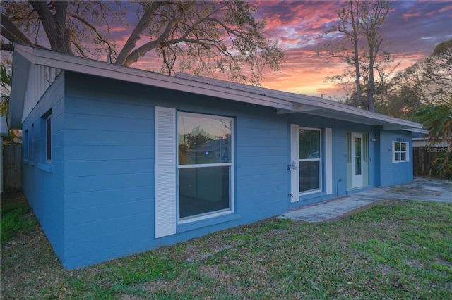 rear view of house featuring concrete block siding, fence, a patio, and a lawn