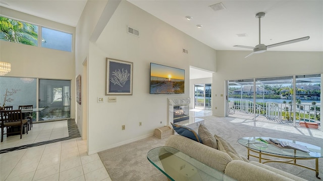 living area featuring light tile patterned floors, high vaulted ceiling, visible vents, baseboards, and a glass covered fireplace