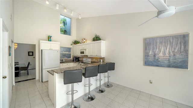 kitchen featuring white appliances, tasteful backsplash, a towering ceiling, a peninsula, and a kitchen bar