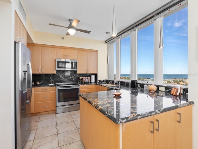 kitchen featuring a peninsula, a sink, appliances with stainless steel finishes, decorative backsplash, and dark stone countertops