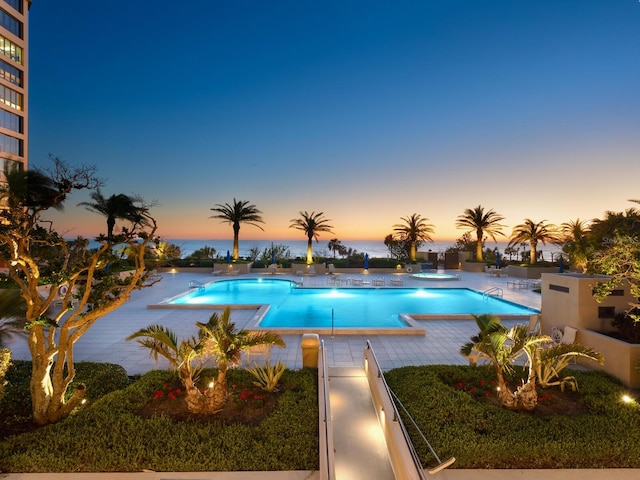 pool at dusk with a patio area and a community pool