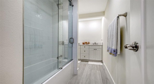 full bath featuring baseboards, bath / shower combo with glass door, wood finished floors, and vanity