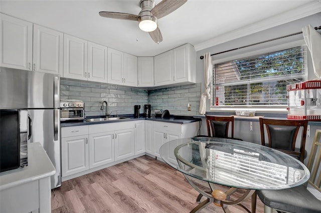 kitchen featuring tasteful backsplash, light wood-style floors, freestanding refrigerator, white cabinetry, and a sink