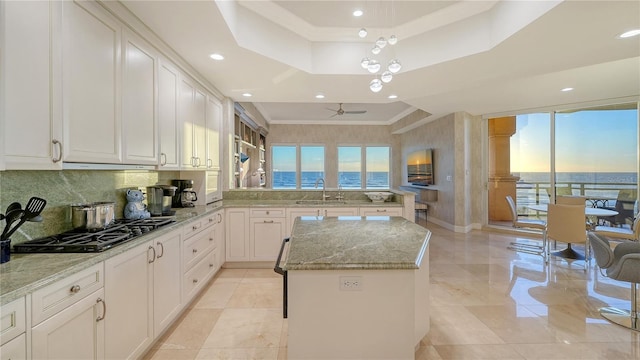 kitchen featuring a kitchen island, light stone countertops, a tray ceiling, ornamental molding, and gas cooktop