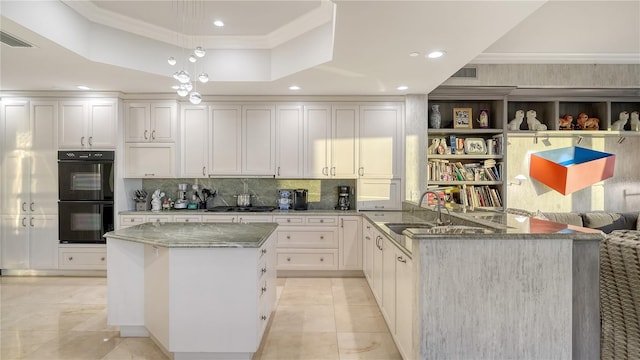 kitchen with a sink, a tray ceiling, stone counters, and dobule oven black