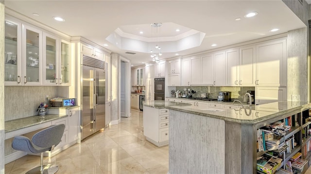 kitchen featuring stainless steel built in refrigerator, dobule oven black, a tray ceiling, tasteful backsplash, and crown molding