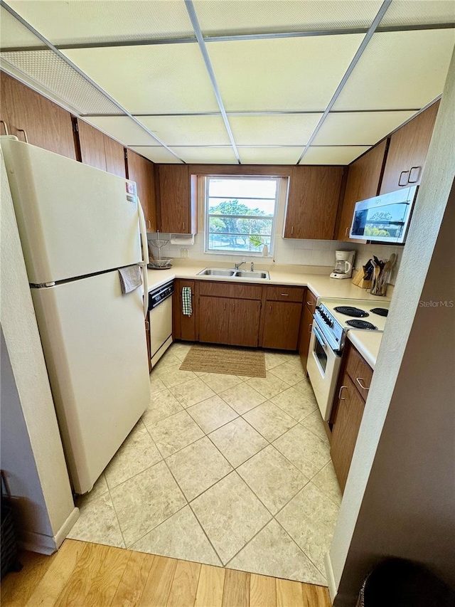 kitchen featuring white appliances, a sink, light countertops, a paneled ceiling, and brown cabinets