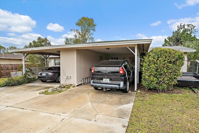 view of parking / parking lot with an attached carport, concrete driveway, and fence