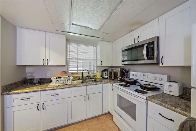 kitchen with stainless steel microwave, light tile patterned floors, electric stove, white cabinetry, and a sink