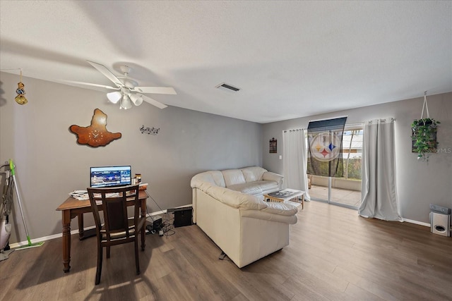 living area featuring a textured ceiling, wood finished floors, visible vents, and baseboards