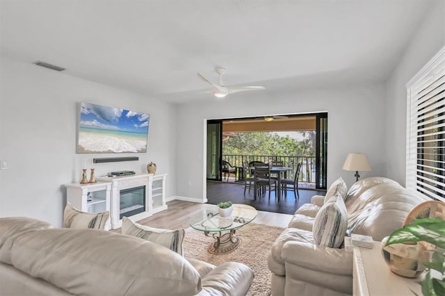 living room with visible vents, a ceiling fan, a glass covered fireplace, wood finished floors, and baseboards