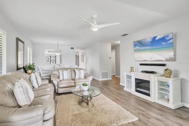 living area with a glass covered fireplace, visible vents, ceiling fan, and wood finished floors