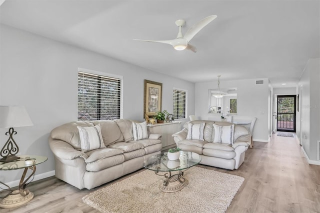 living room featuring light wood finished floors, baseboards, visible vents, and a ceiling fan