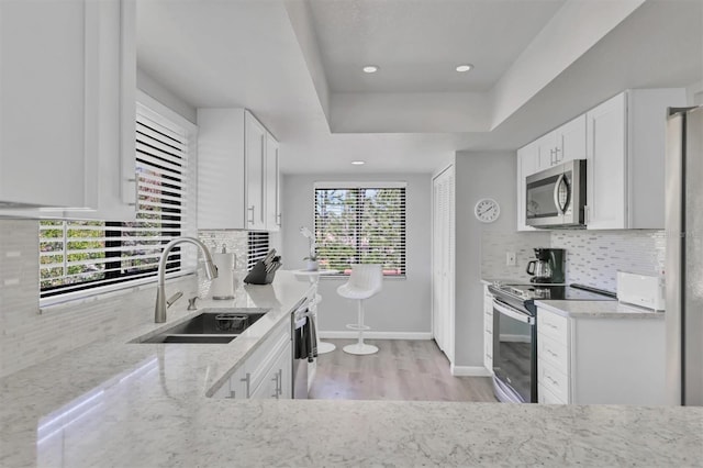 kitchen featuring light stone counters, a raised ceiling, appliances with stainless steel finishes, white cabinets, and a sink