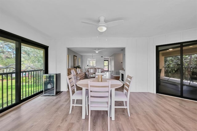 dining room featuring light wood finished floors, ceiling fan, a decorative wall, and beverage cooler