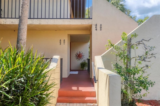 view of exterior entry featuring a balcony and stucco siding