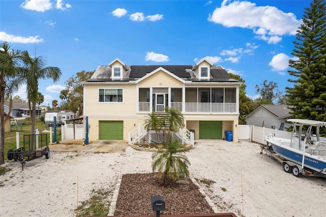 view of front of home with driveway, a sunroom, roof mounted solar panels, and a gate