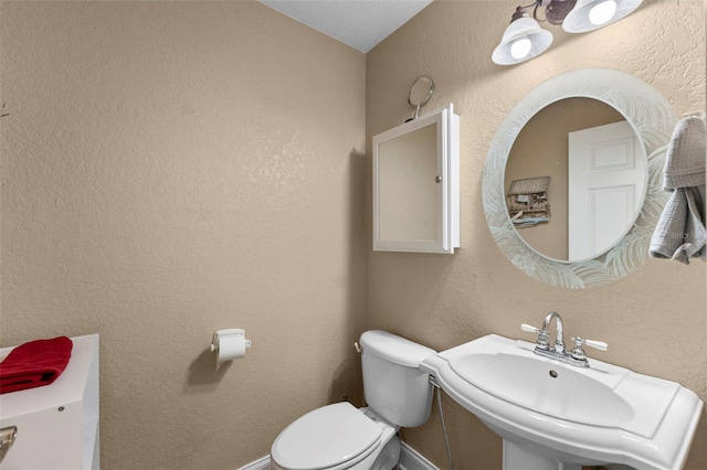 half bathroom with toilet, baseboards, a sink, and a textured wall