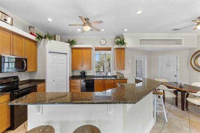 kitchen with brown cabinets, ornamental molding, ceiling fan, black appliances, and a kitchen breakfast bar