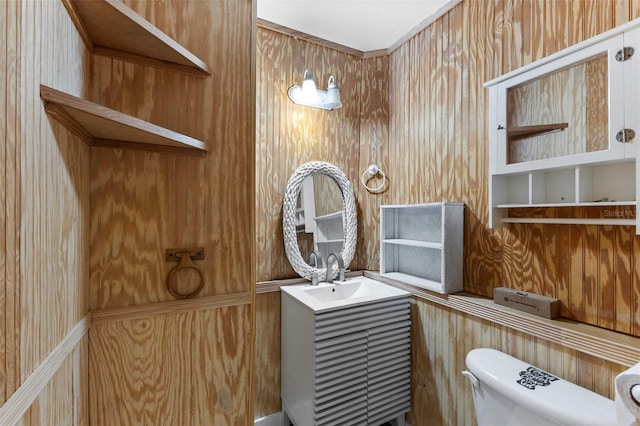 bathroom featuring toilet, wooden walls, and a sink