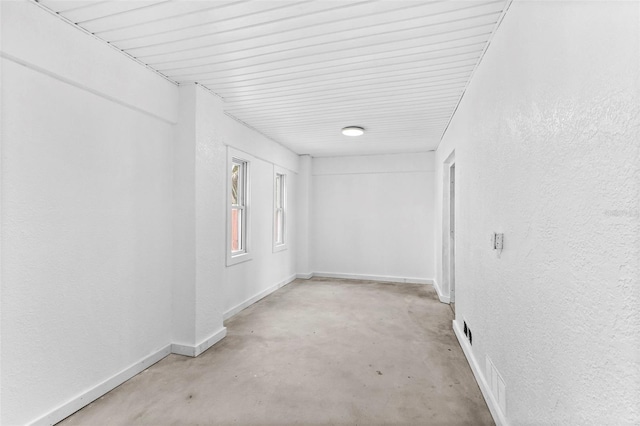 spare room with concrete flooring, a textured wall, and baseboards