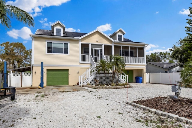 raised beach house with a sunroom, fence, an attached garage, and stairs