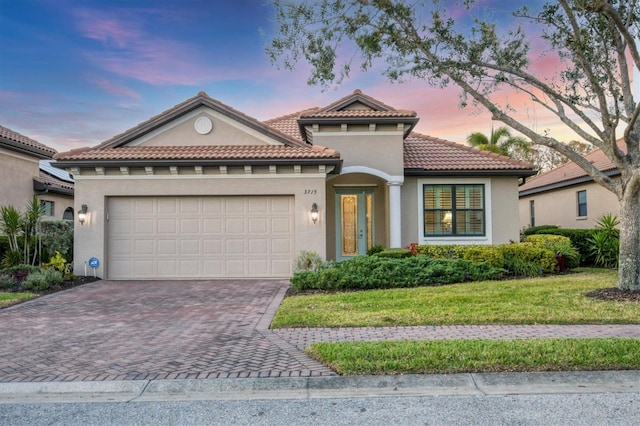 mediterranean / spanish house featuring a garage, a lawn, a tiled roof, decorative driveway, and stucco siding