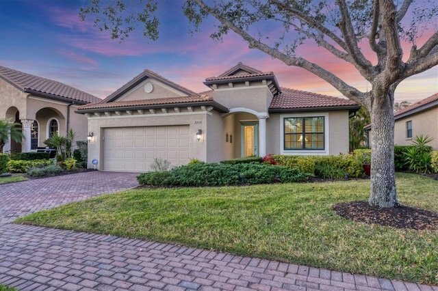 mediterranean / spanish house with a garage, a tile roof, decorative driveway, a front lawn, and stucco siding