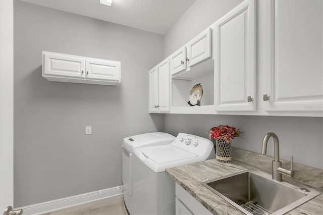 washroom with baseboards, cabinet space, a sink, and washing machine and clothes dryer