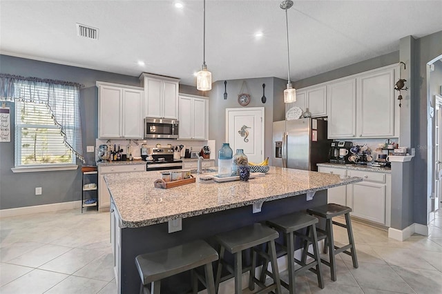 kitchen featuring a kitchen island with sink, visible vents, a kitchen breakfast bar, appliances with stainless steel finishes, and backsplash