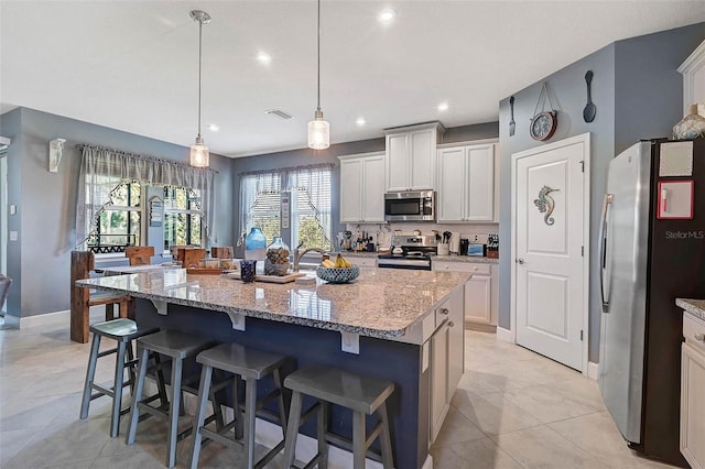 kitchen with a center island with sink, decorative backsplash, a kitchen breakfast bar, light stone countertops, and stainless steel appliances