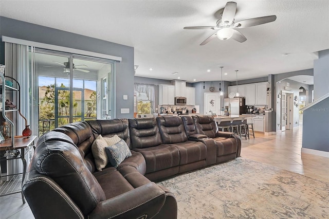 living area with light tile patterned floors, arched walkways, baseboards, ceiling fan, and a textured ceiling