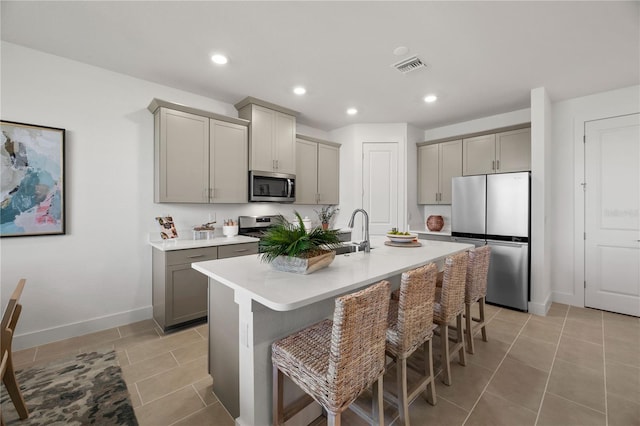 kitchen featuring visible vents, appliances with stainless steel finishes, a breakfast bar, gray cabinetry, and a sink