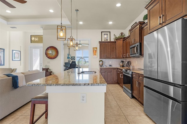 kitchen featuring light tile patterned floors, appliances with stainless steel finishes, open floor plan, a sink, and a kitchen breakfast bar