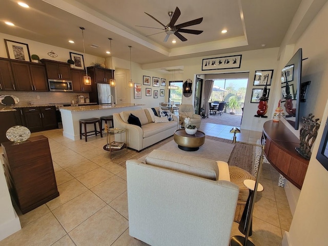 living area featuring a ceiling fan, a tray ceiling, recessed lighting, and light tile patterned floors