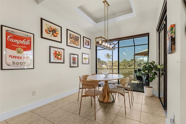 dining area featuring a tray ceiling, light tile patterned floors, baseboards, and an inviting chandelier