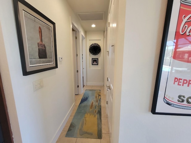 hall with light tile patterned flooring, attic access, and baseboards